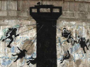 Un murale raffigurante bambini che usano una torre di guardia dell’esercito israeliano come giostra, dipinto dall’artista britannico Banksy, visibile su un muro lungo la strada principale di Beit Lahiya, nella Striscia di Gaza settentrionale, il 17 febbraio 2015. Foto: Adel Hana